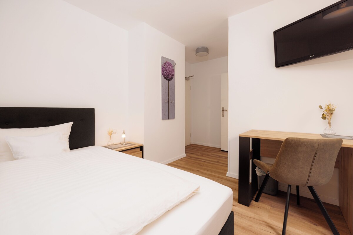 Een hotelkamer met een bed, een bureau, een stoel, een televisie en een deur naar een badkamer.