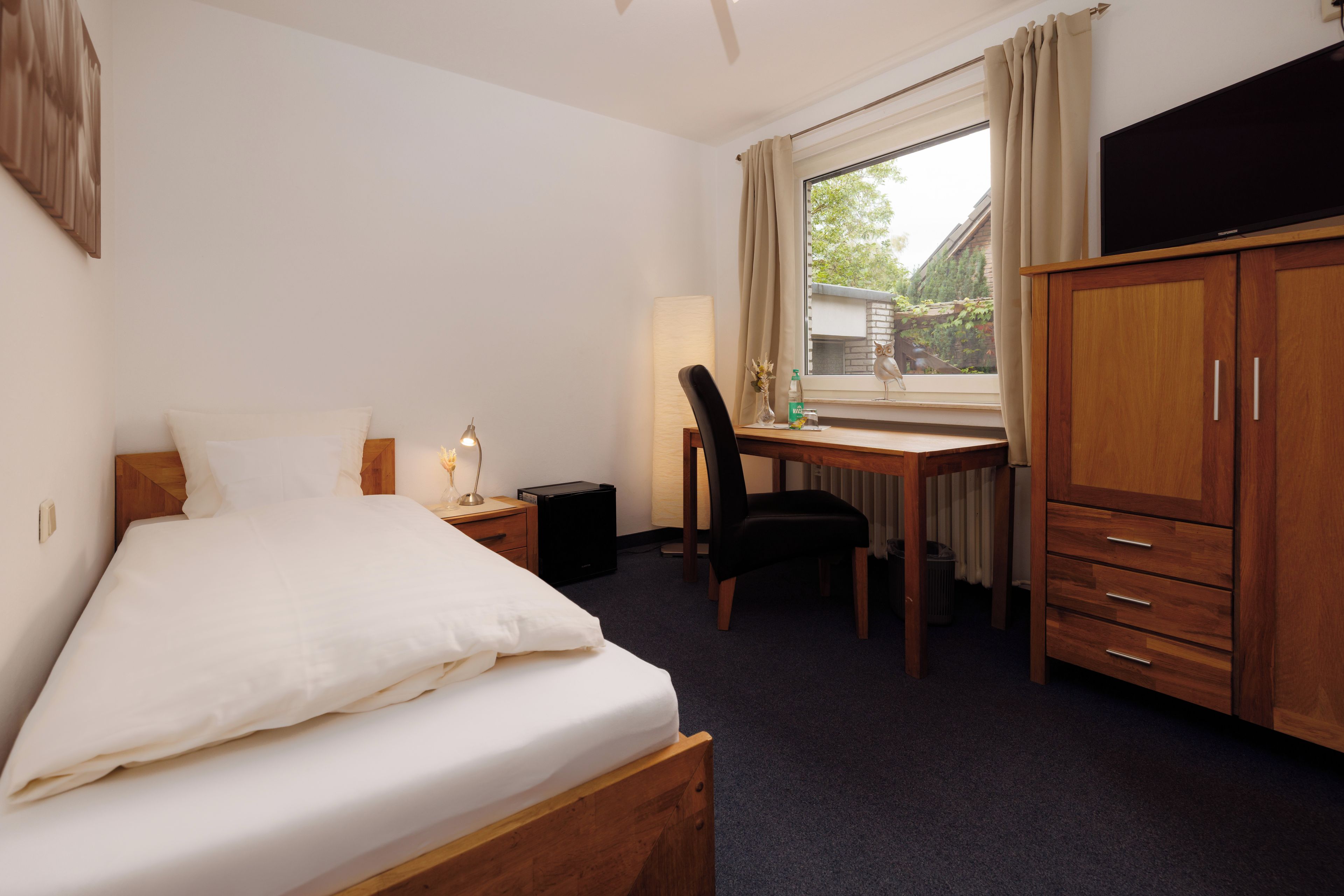 A hotel room with a bed, a desk, a chair, a TV, and a wardrobe.