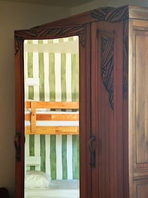 A wooden wardrobe with intricate carvings and a partially open door revealing a bed with a striped headboard. - Domaine du Moulin Français - By the Fireplace (Champougny)