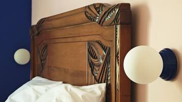 Een bed met een houten hoofdbord met ingewikkelde houtsnijwerken, een wit kussen en een rond, aan de muur bevestigd lampje.