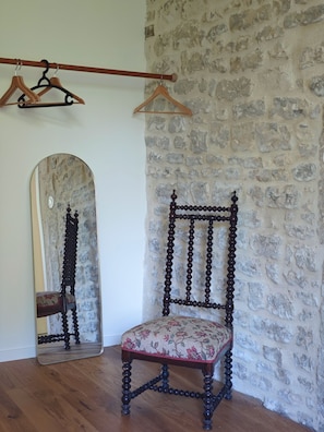 A room with a wooden chair, a mirror, and a stone wall. - Domaine du Moulin Français - By the Fireplace (Champougny)