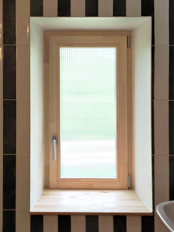 Un baño con puerta de madera, un banco y pared de azulejos.