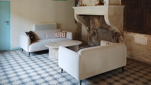 Ein Wohnzimmer mit einer Couch, einem Sessel und einem Couchtisch, einem Kamin aus Stein und fugenreichen Fliesen.