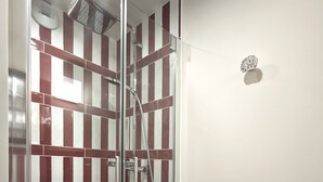 Eine gläserne Duschkabine mit einer Wand aus rot-weiß gestreiften Fliesen, einer Brause und einem Handbrausehalter.