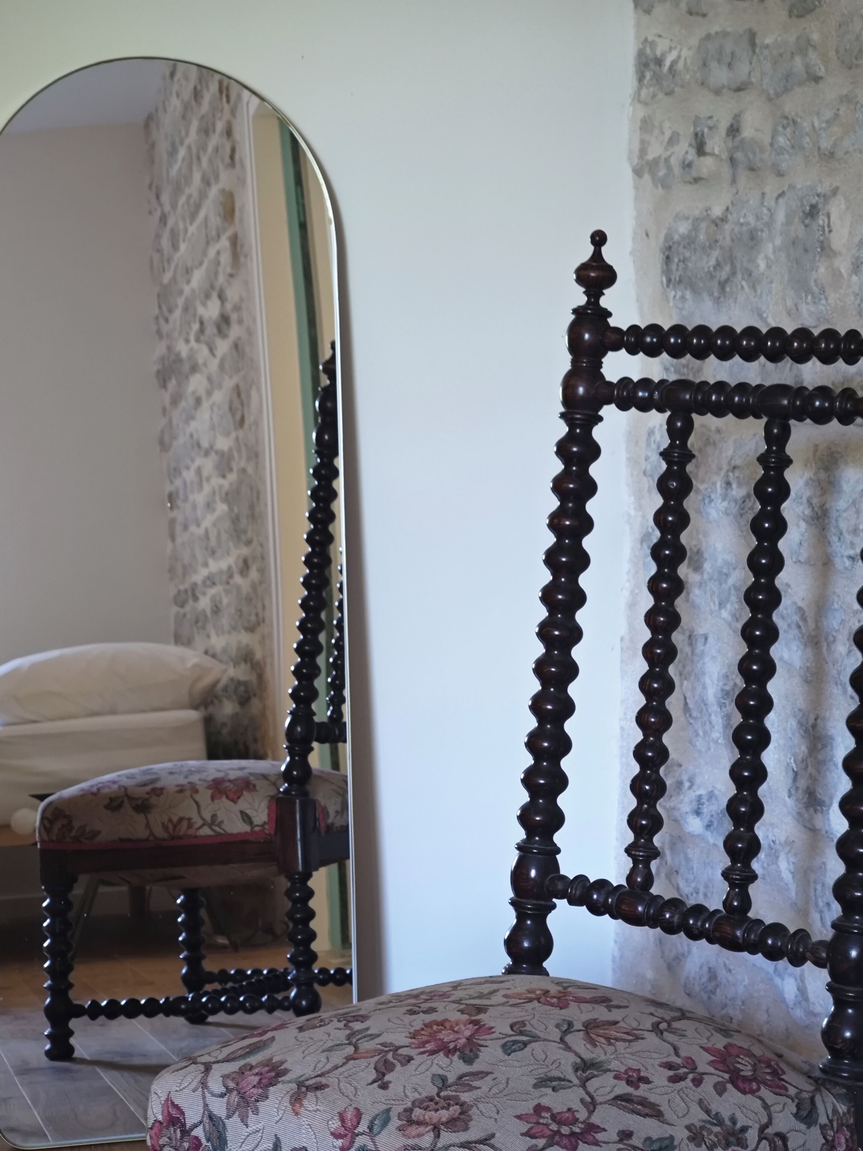 Ein Zimmer mit einem Bett, einem Sessel und einem Spiegel, der eine Wand mit strukturierter Oberfläche zeigt.