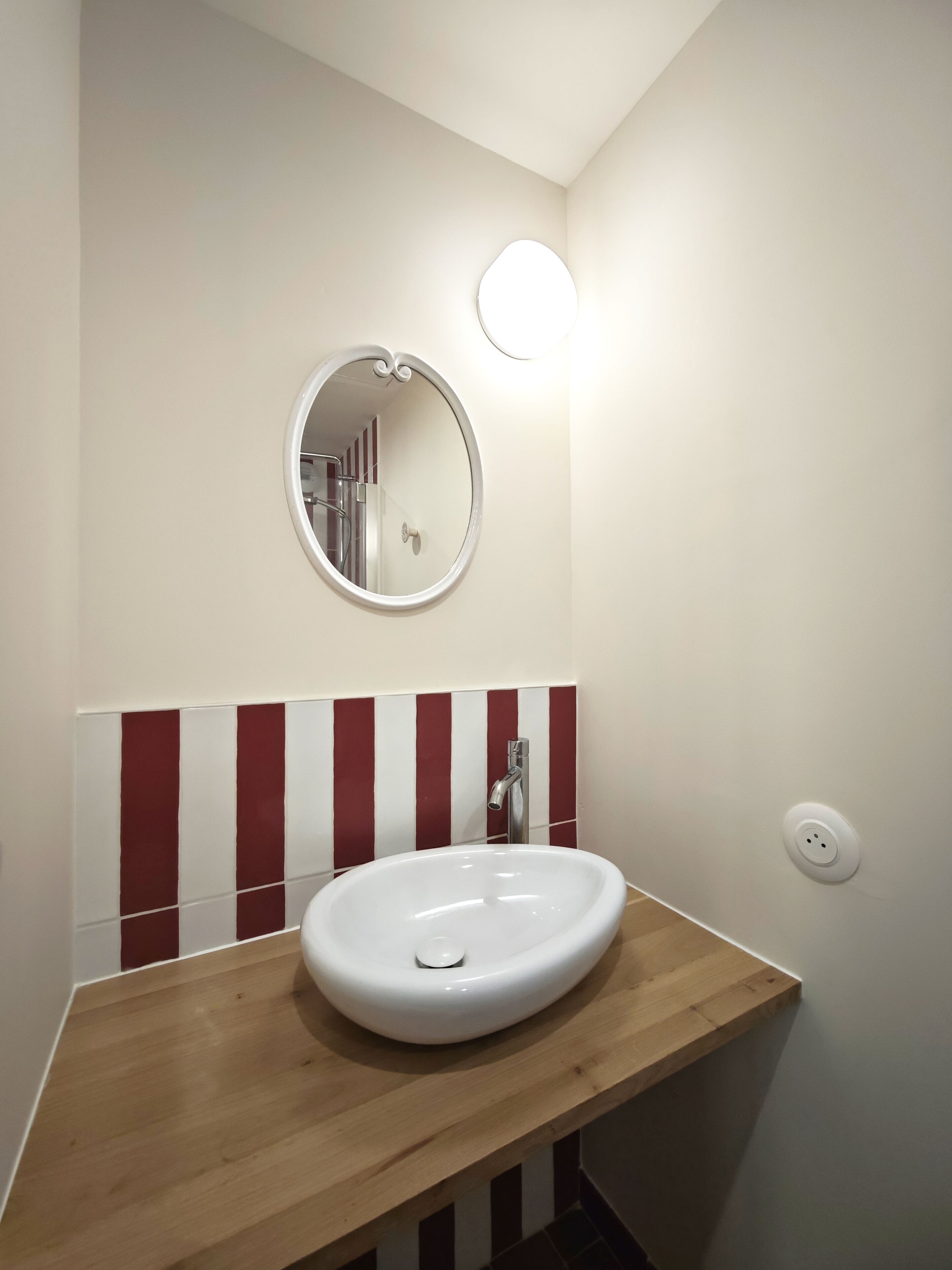 Une salle de bain avec un lavabo blanc, un miroir rond et un mur à rayures rouges et blanches.