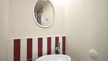 Une salle de bain avec un lavabo blanc, un miroir rond et un mur à rayures rouges et blanches.