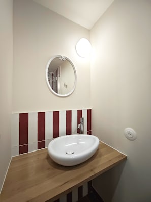 Un baño con un lavabo blanco, un espejo redondo y una pared a rayas rojas y blancas.