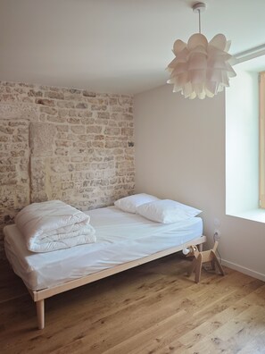 A single bed with a wooden frame, white bedding, and a stone wall. - Domaine du Moulin Français - By the Fireplace (Champougny)