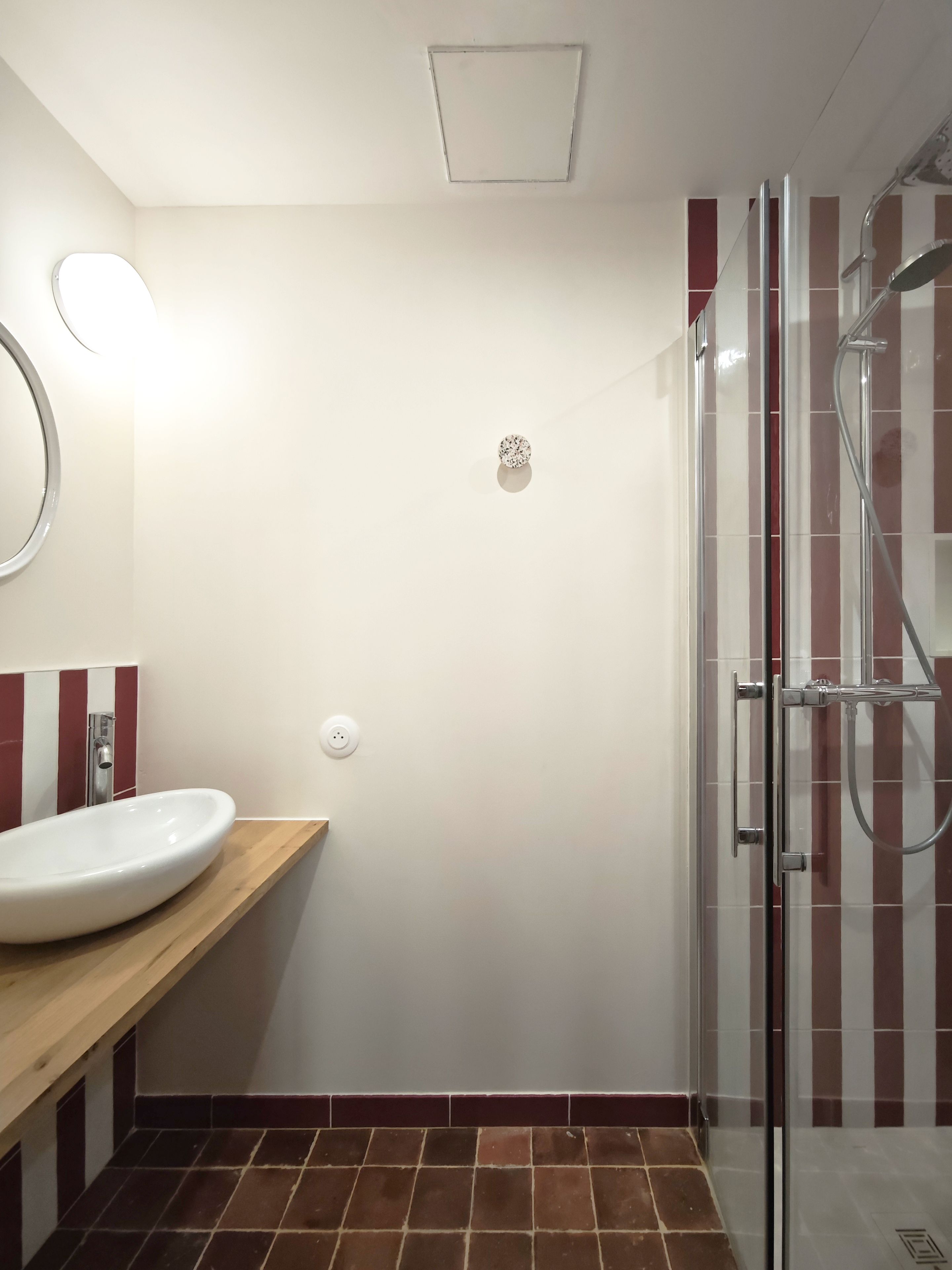 Een badkamer met een wit wastafelmeubel, een spiegel, een douche met glazen deur en een betegelde vloer.