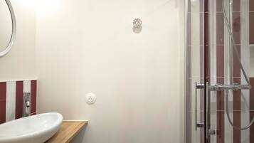 Een badkamer met een wit wastafelmeubel, een spiegel, een douche met glazen deur en een betegelde vloer.
