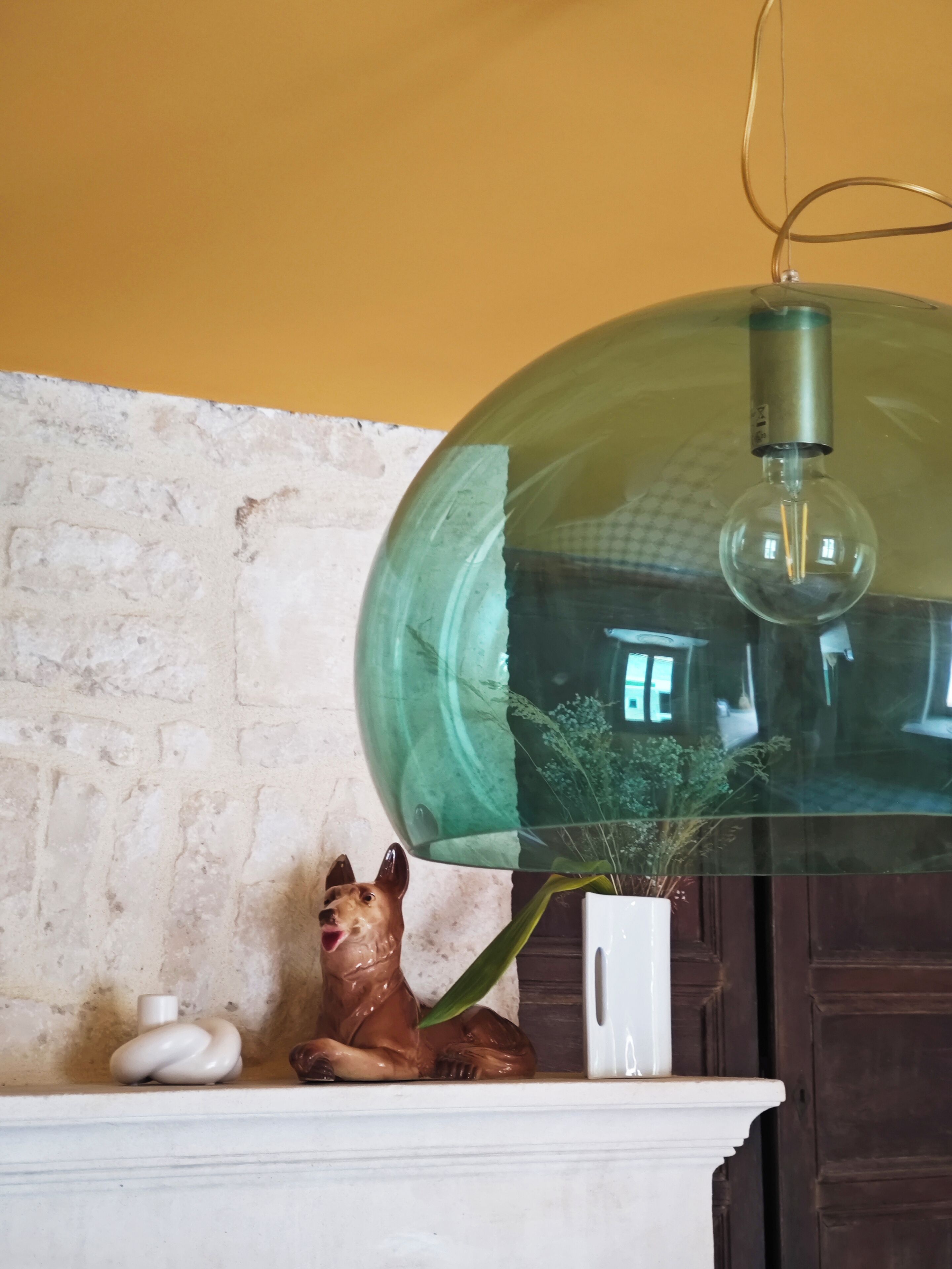 A room with a white brick wall, a white fireplace mantel, and a large green glass pendant light.