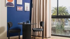 A room with a blue wall, a round table with chairs, a window with curtains, and artwork on the wall.