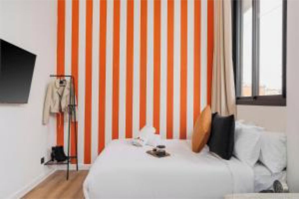 Une chambre d’hôtel avec un mur à rayures, un lit avec des oreillers, une table de chevet et une fenêtre.