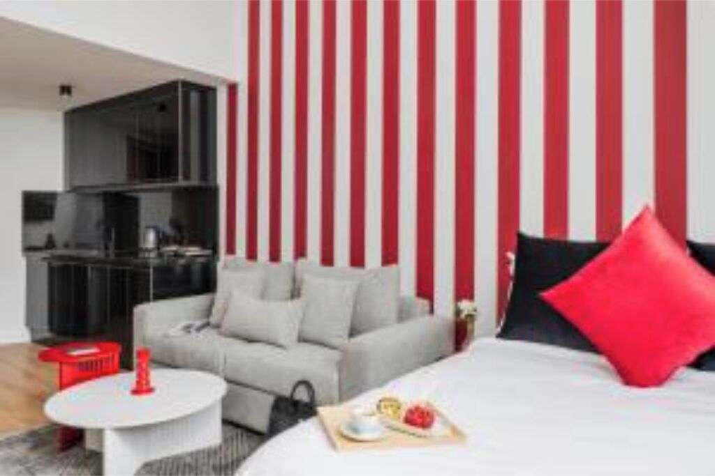 Une chambre d’hôtel moderne avec un lit, un canapé, une petite table et un mur à rayures rouges.