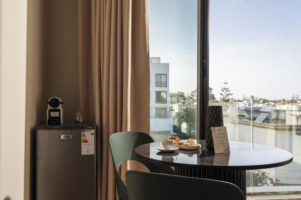 Une chambre d’hôtel équipée d’une table à manger, de chaises, d’un minibar et offrant une vue sur les bâtiments et l’eau.