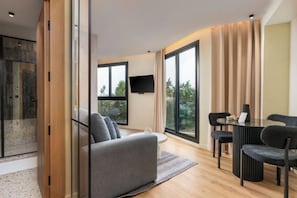 A modern living room with a sofa, a dining table, and chairs. There is a TV mounted on the wall and a large window providing a view of the outdoors. - The corner by goodmove (Casablanca)