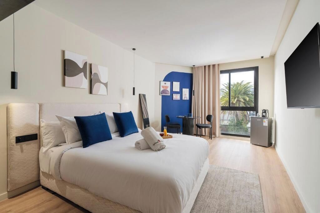 Habitación de hotel con cama, escritorio, silla, televisor y balcón con vistas.