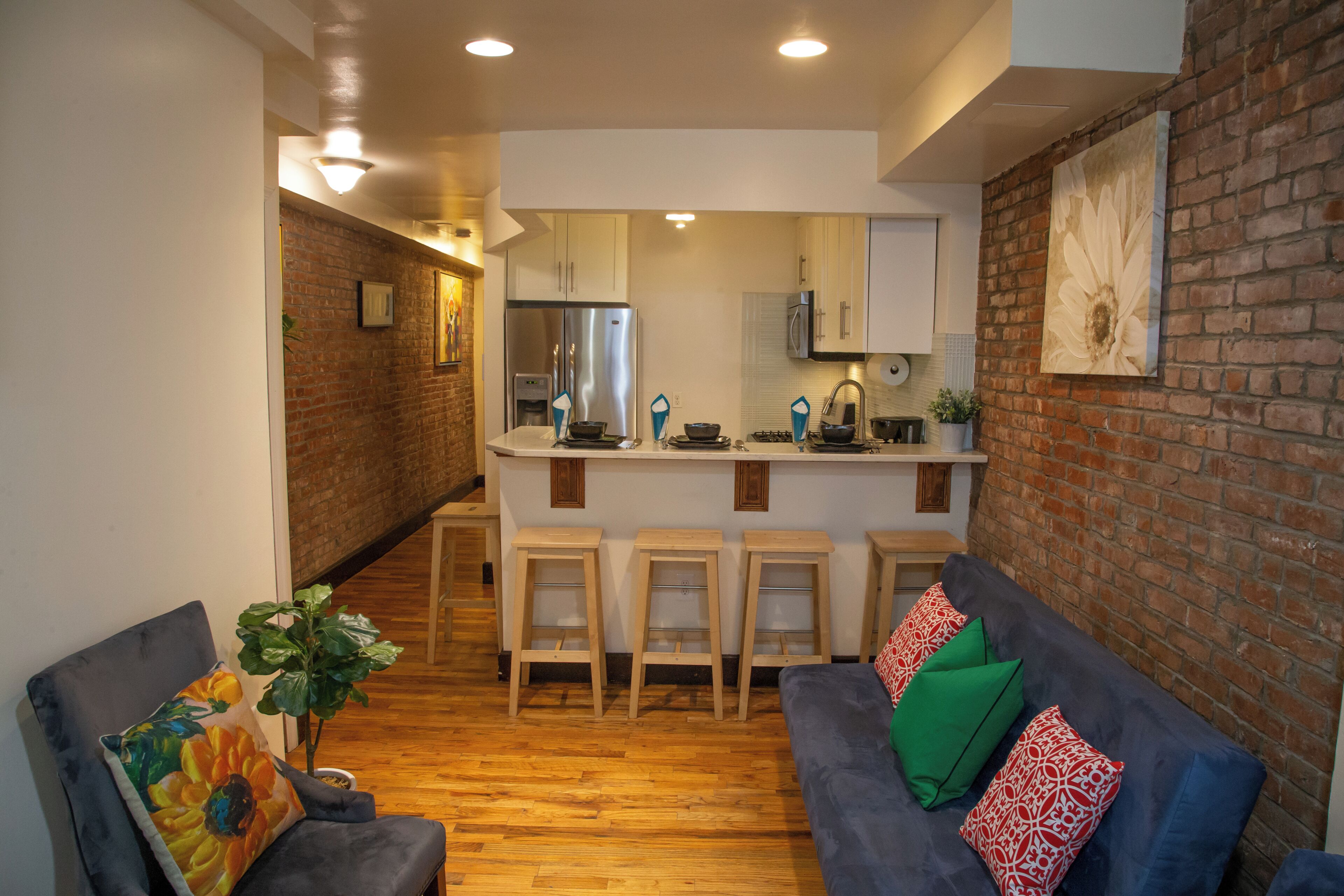 A modern kitchen with a central island, bar stools, and a brick accent wall.