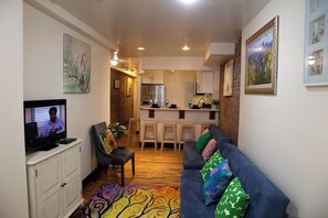 A living room with a television, a sofa with patterned cushions, a coffee table, and a kitchen area in the background. - Brownstone Cove (New York)