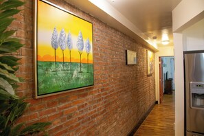 A hallway with a brick wall, a painting of trees, and a refrigerator. - Brownstone Cove (New York)
