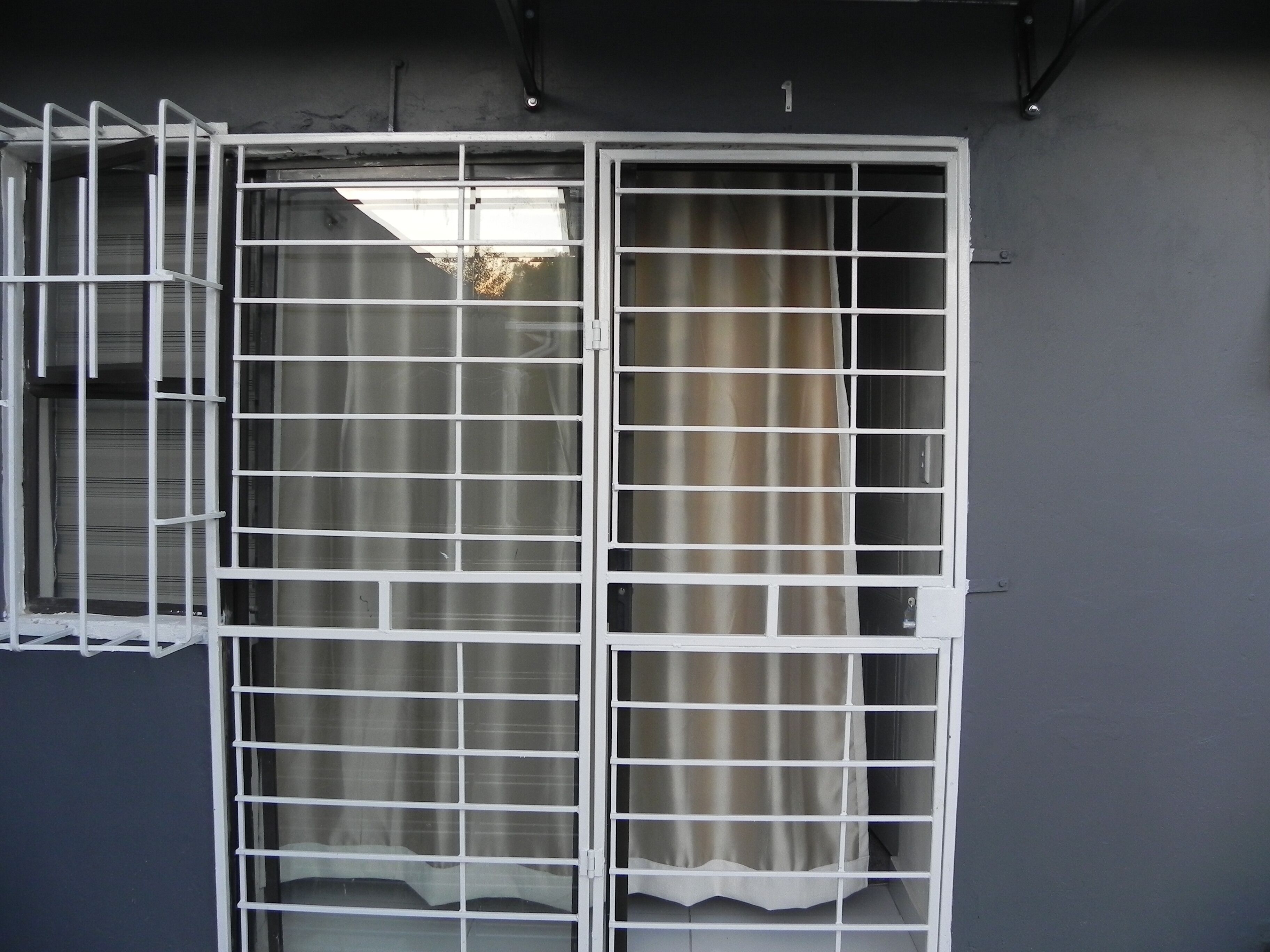 A window with a metal grid design, a curtain, and a wall with a number '1' sign.
