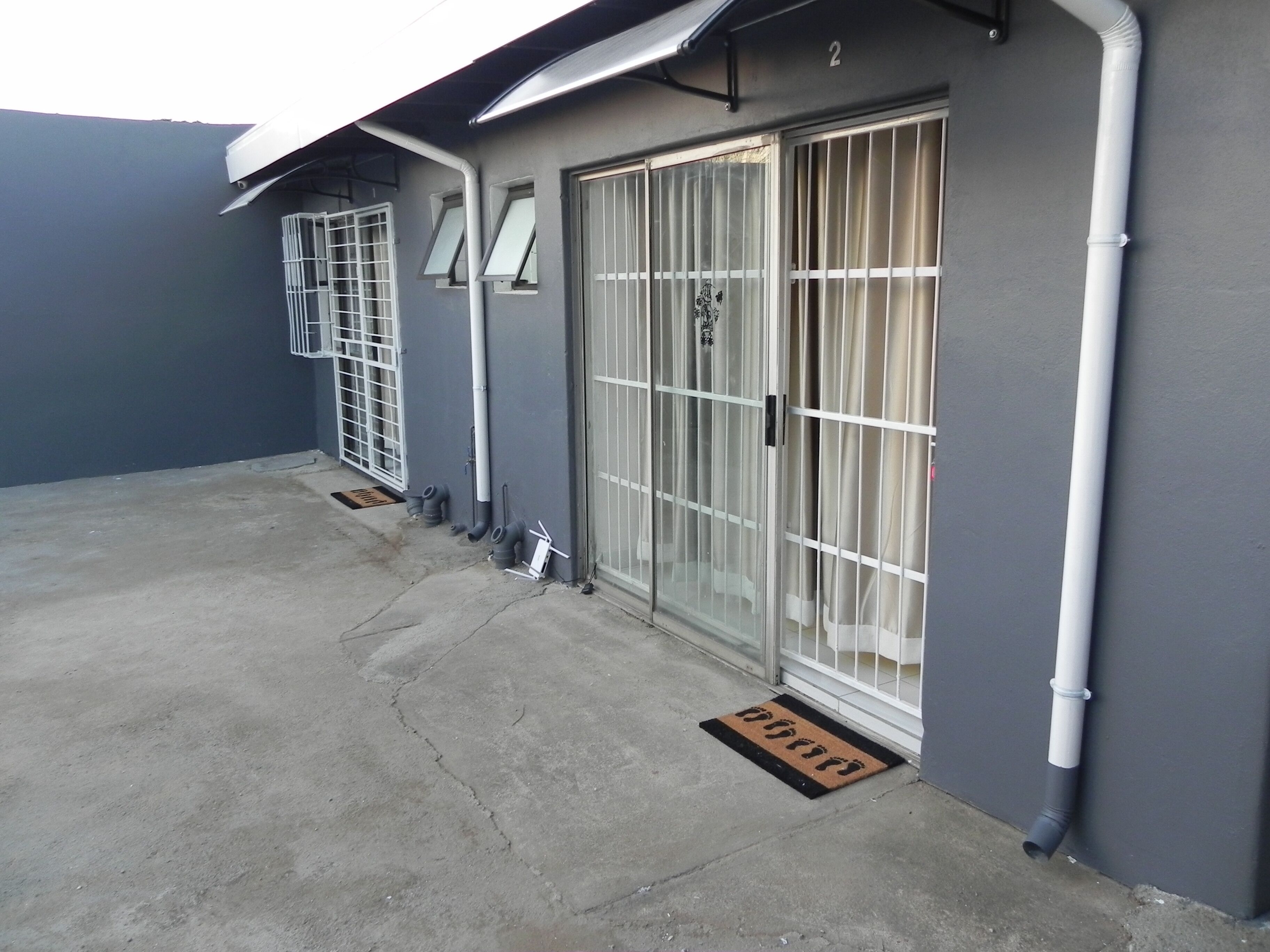 A building exterior with a grey wall, a metal gate, and a doormat.