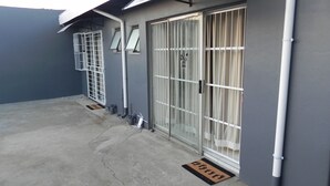 A building exterior with a grey wall, a metal gate, and a doormat. - OZ Guest Villa (Johannesburg South)