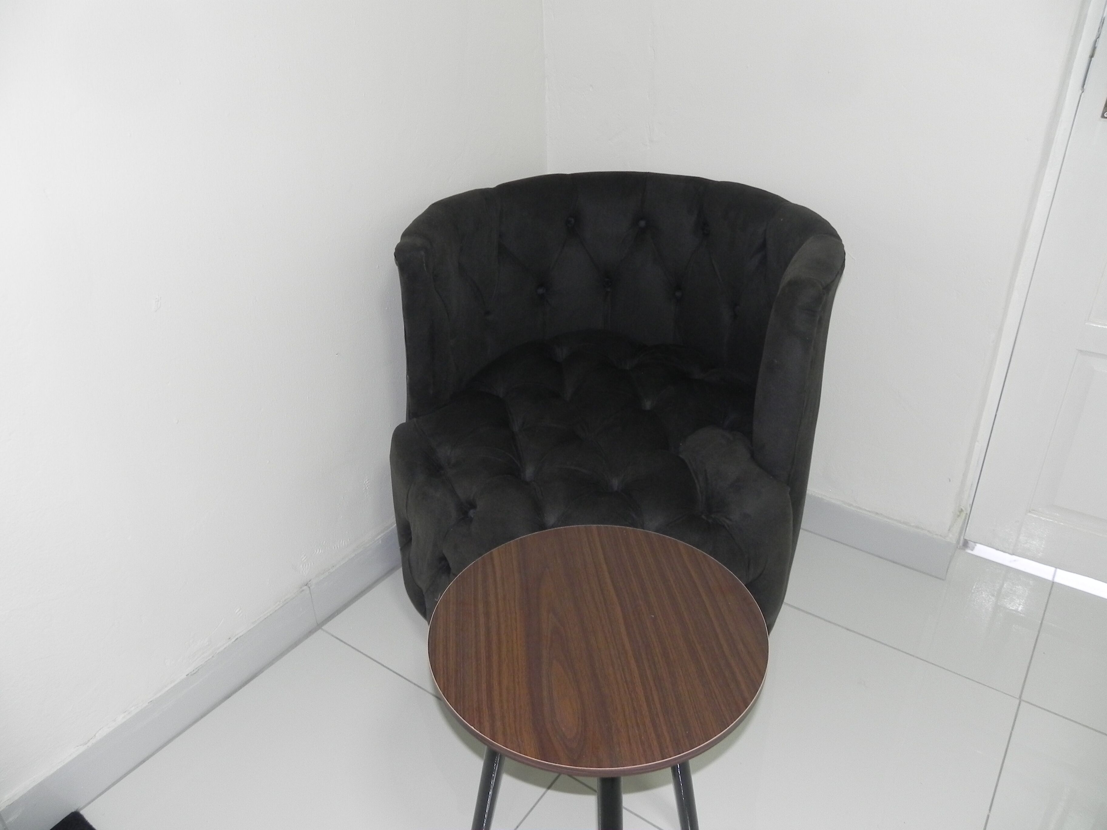 A black tufted armchair with a round wooden table in front of it.