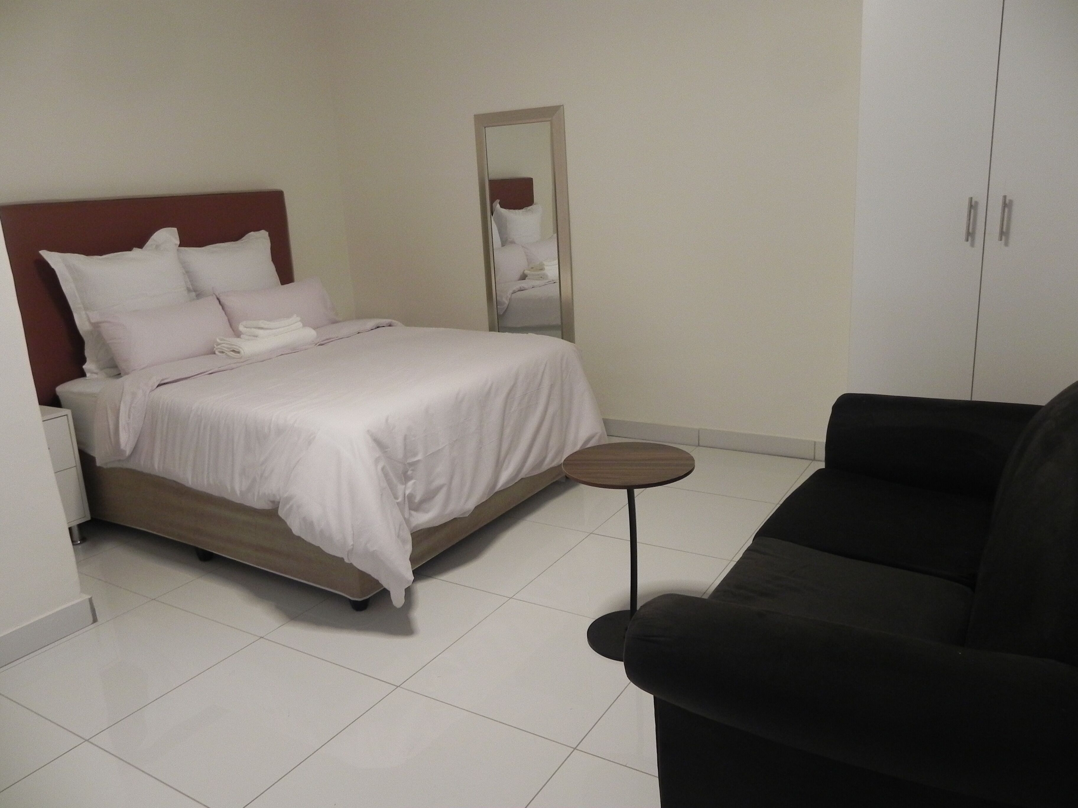A hotel room with a bed, a small round table, a black sofa, and a wardrobe.