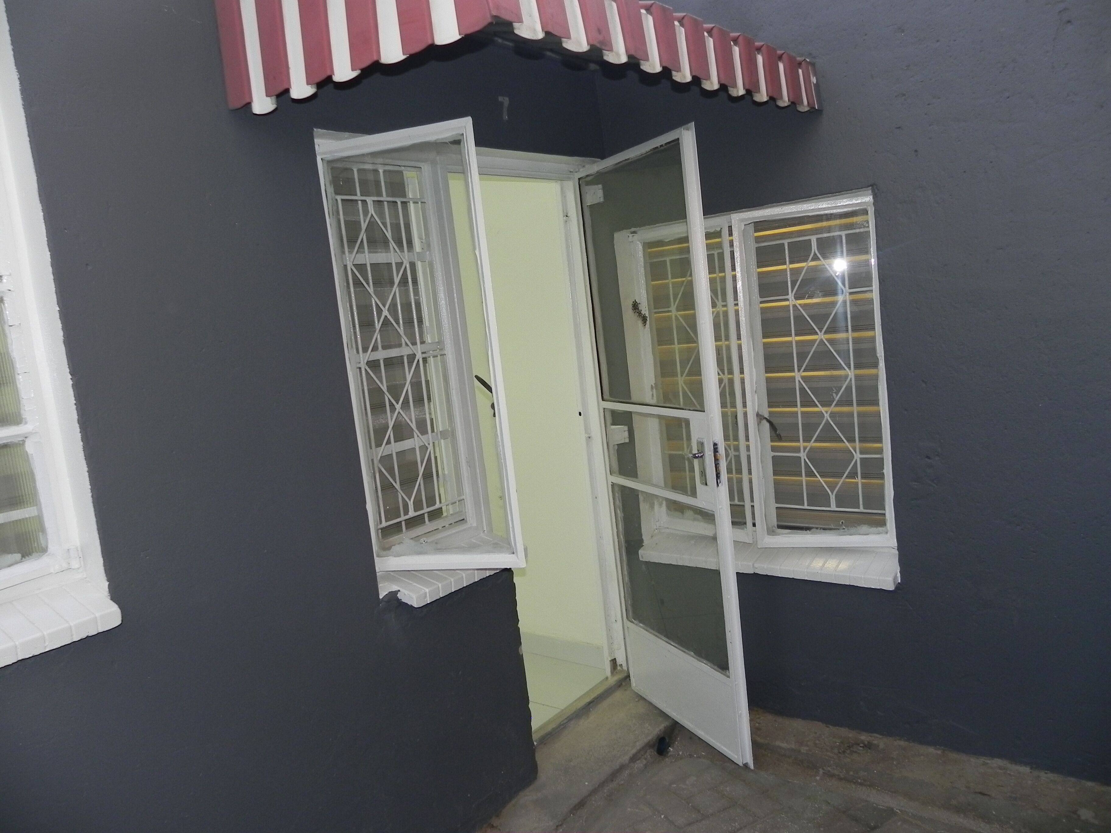 A doorway with two open windows, one with a metal grille and one with a mesh screen, leading to a room with a tiled floor.