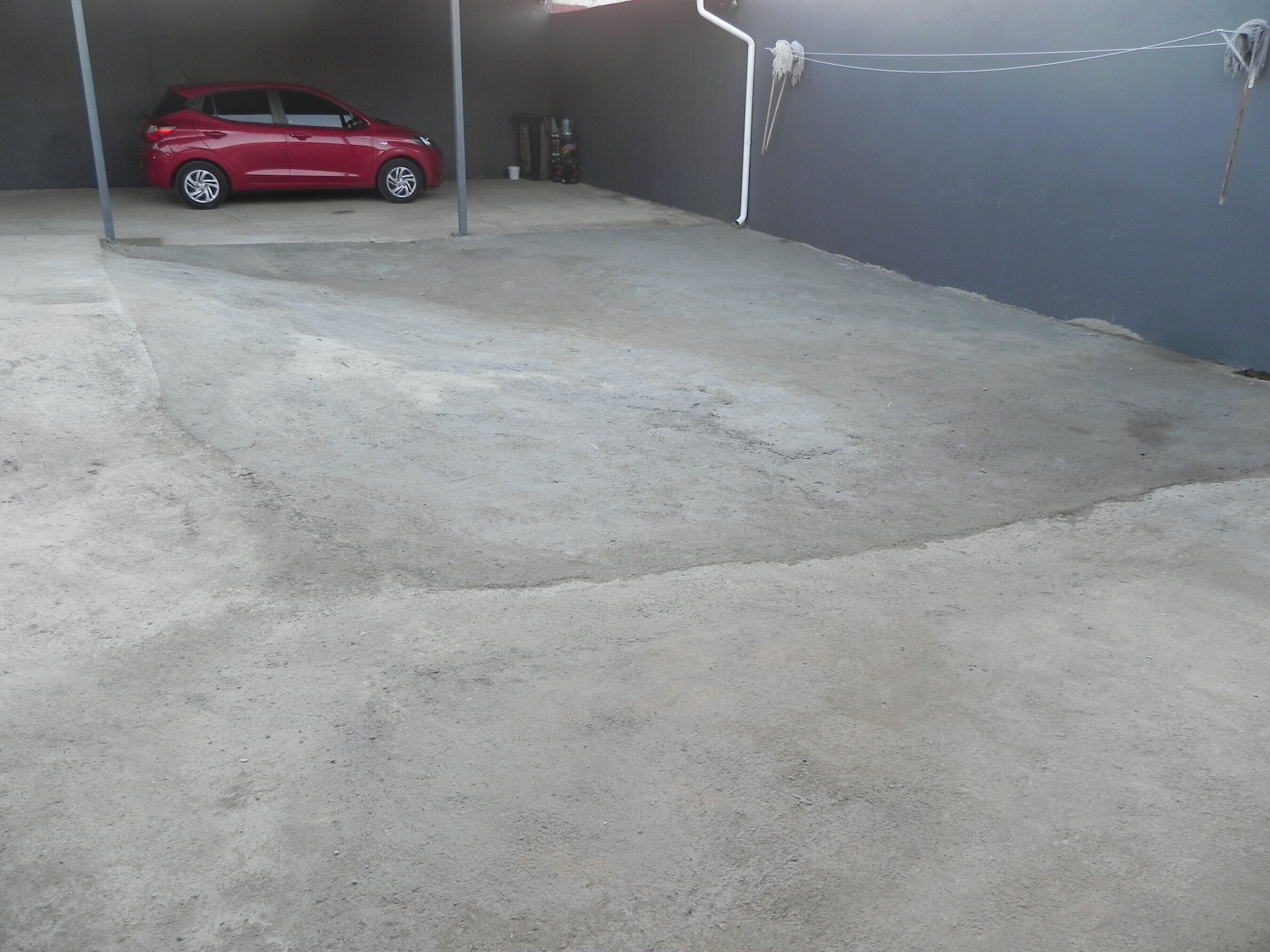 A red car parked in a garage with a concrete floor and a grey wall.