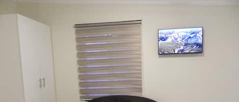 A room with a black sofa, a small round table, a white wardrobe, a window with blinds, and a framed picture on the wall.