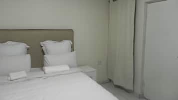 A hotel room with a bed, pillows, a nightstand, a curtain, and a door.