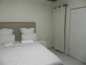 Ein Hotelzimmer mit Bett, Kissen, Nachttisch, Vorhang und Tür.