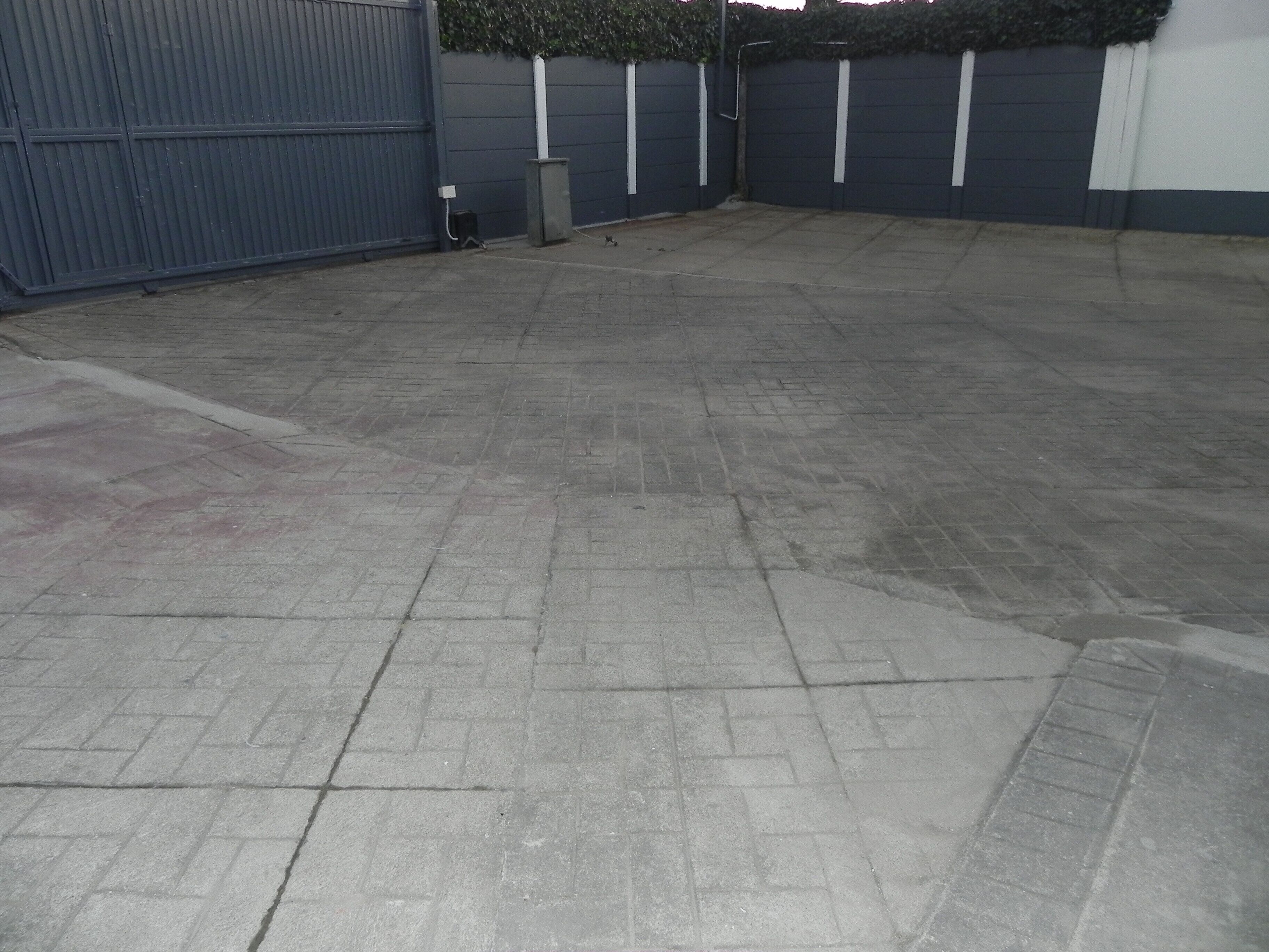 A paved outdoor area with a blue gate, a trash bin, and a wall with vertical lines.