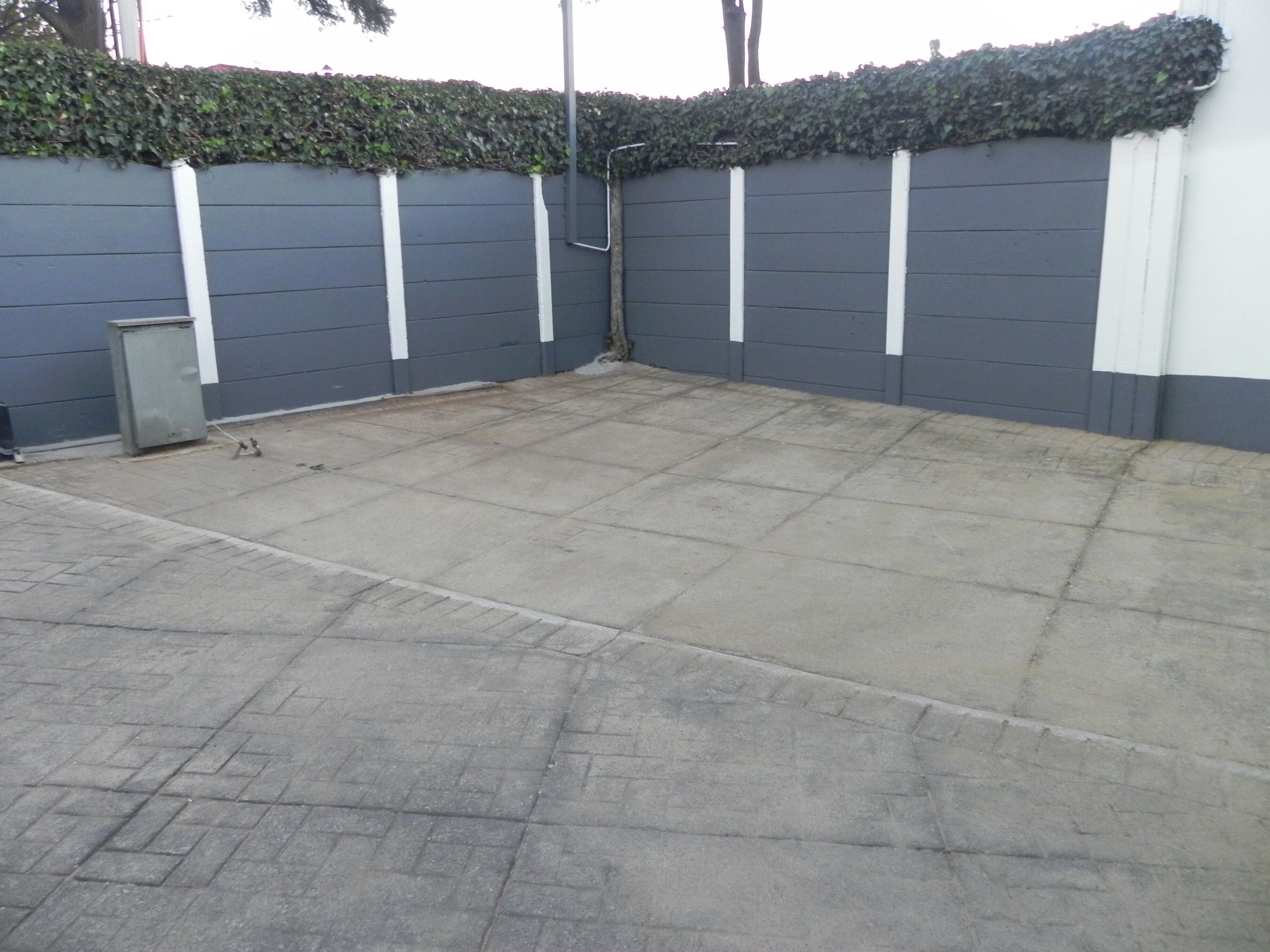 A concrete parking area with a grey wall and a white trim.