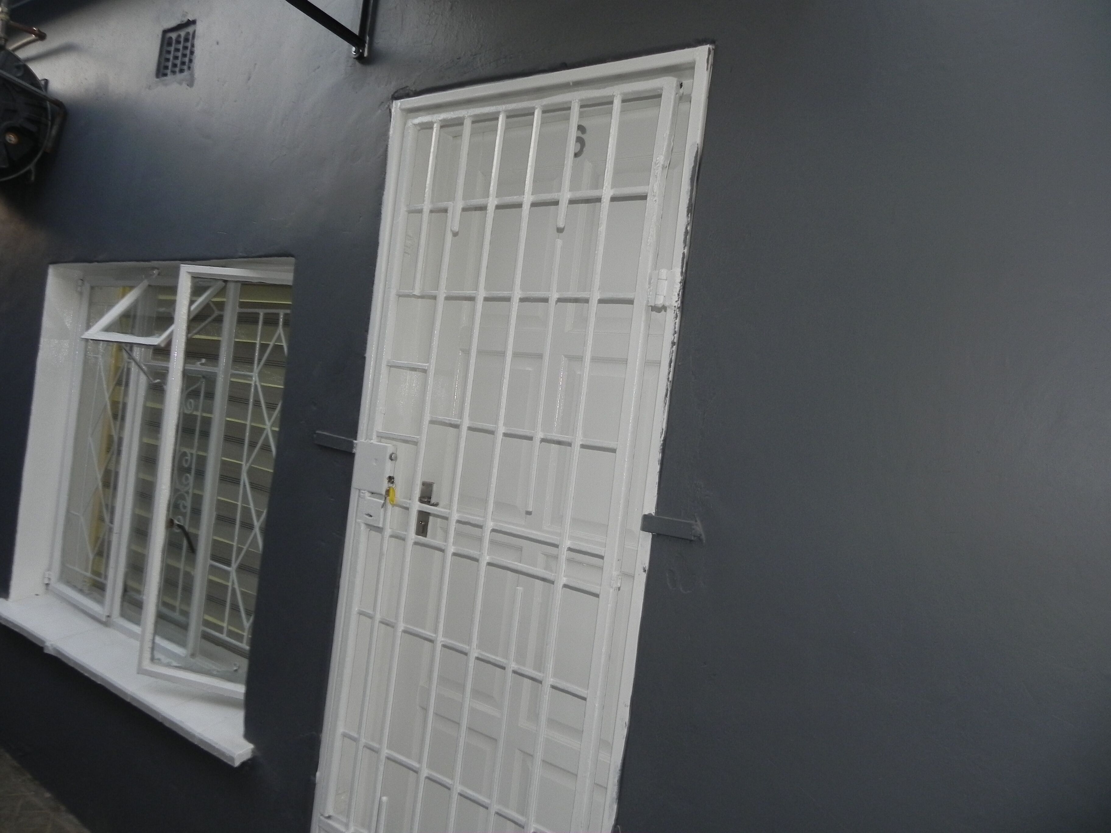 A white door with a grid pattern, a window with a metal grid, and a grey wall.