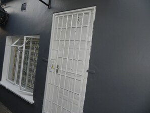 Eine weiße Tür mit Gittermuster, ein Fenster mit Metallgitter und eine graue Wand.