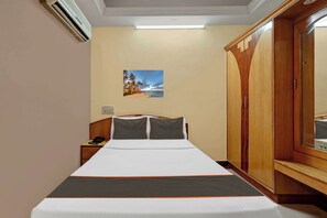 Habitación de hotel con cama, mesita de noche, lámpara, armario y un cuadro colgado en la pared.