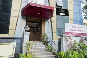 Entrada de un edificio con una escalera, un toldo rojo y un cartel que indica 'Skanda Shelters'.