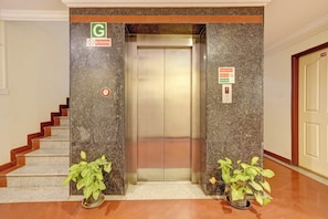 Un ascensor con un cartel de 'No Fumar', un rótulo de seguridad contra incendios y una 'G' que indica un baño unisex.