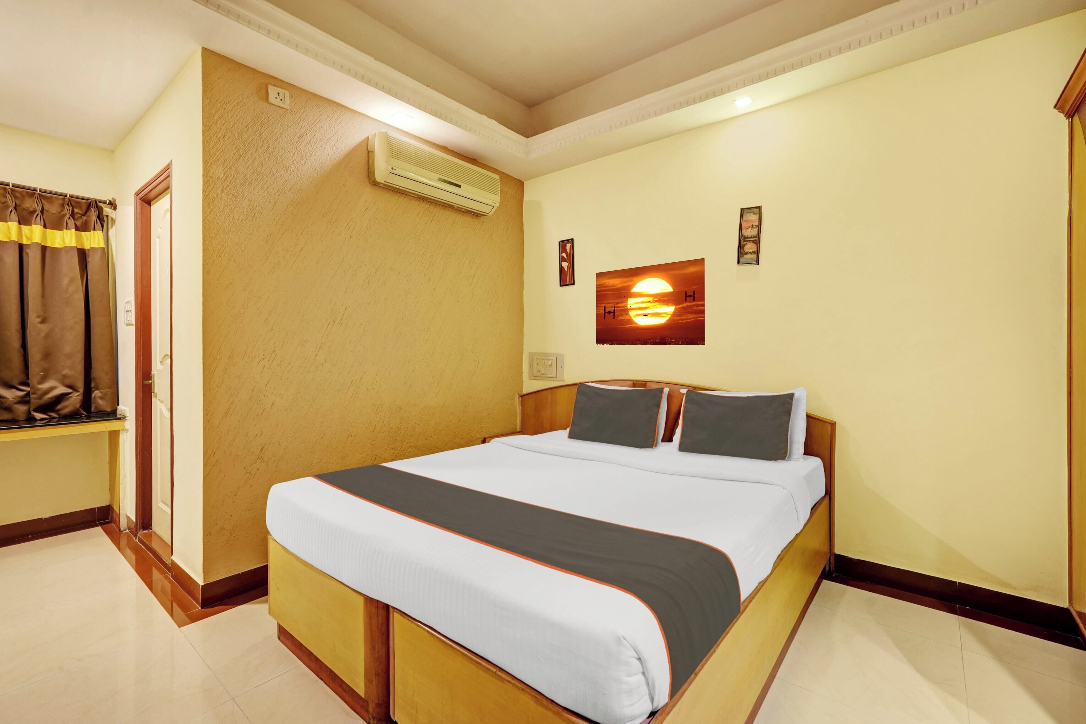 Habitación de hotel con cama, aire acondicionado de pared, ventana con cortinas e imagen colgada en la pared.