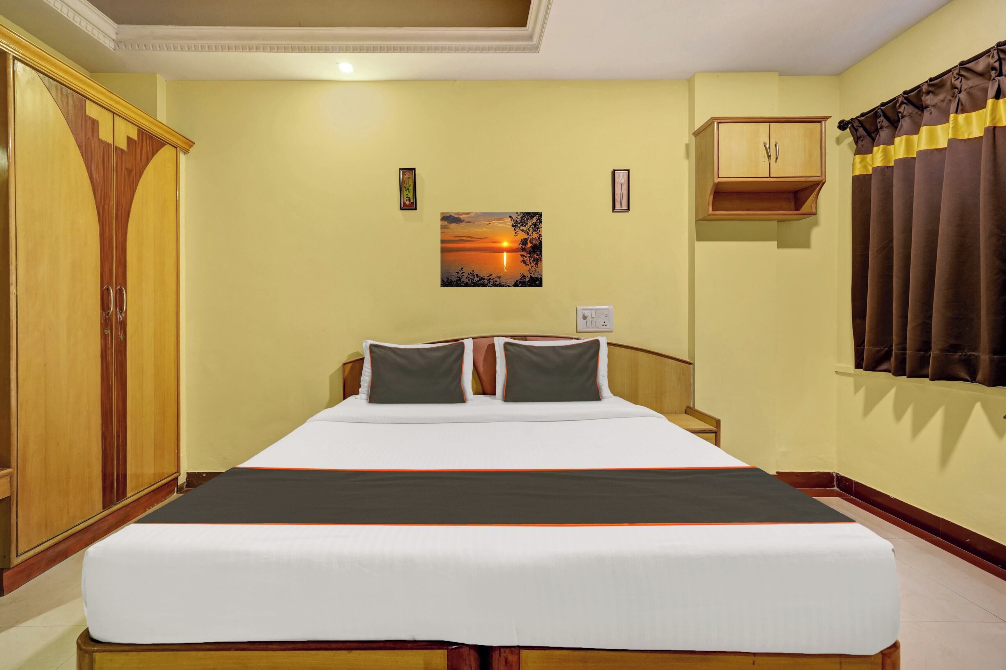 A hotel room with a bed, a wardrobe, a painting, and a window with curtains.