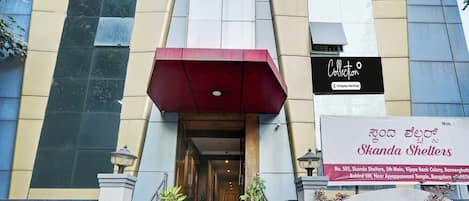 Entrada de un edificio con una escalera que lleva a una puerta, un toldo rojo y un letrero de Skanda Shelters.
