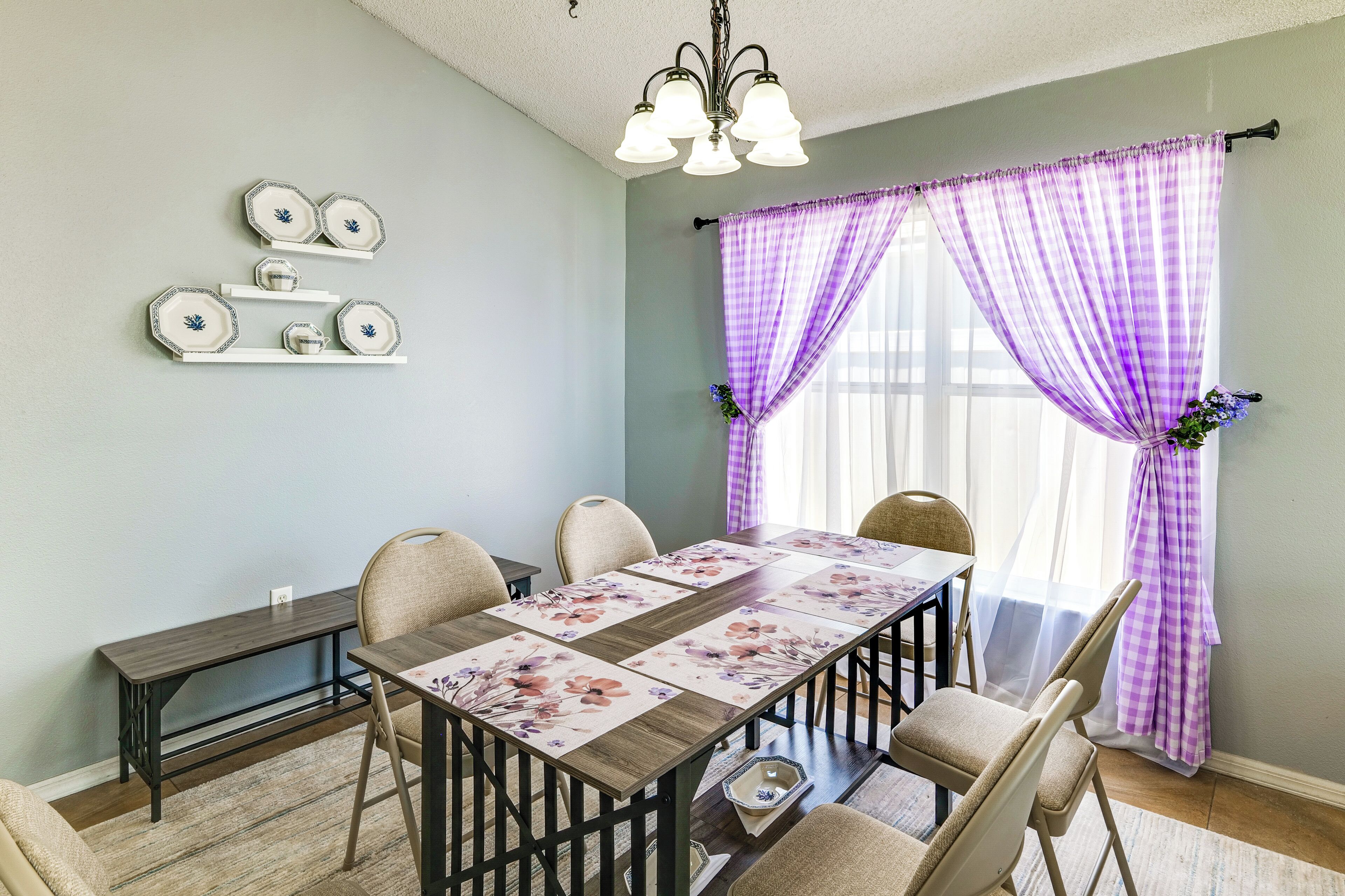 A dining area with a table set for four, chairs, a decorative wall piece, and a window with purple curtains.