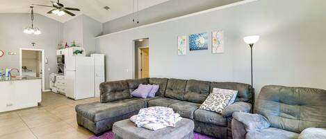 A living room with a grey sectional sofa, a matching ottoman, and a purple rug.