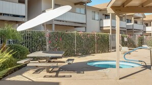 A swimming pool area with a sunshade, lounge chairs, and a fence with climbing plants. - Walkable Tempe Condo < 1 Mi to ASU Campus! (Tempe)