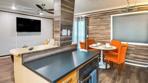 A modern kitchen with a built-in oven, a dining area with orange chairs, and a flat-screen TV mounted on the wall. - Walkable Tempe Condo < 1 Mi to ASU Campus! (Tempe)
