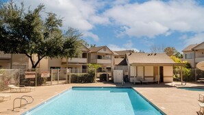 A swimming pool area with a clear sky, a fenced pool, lounge chairs, and a building with a covered seating area. - Walkable Tempe Condo < 1 Mi to ASU Campus! (Tempe)